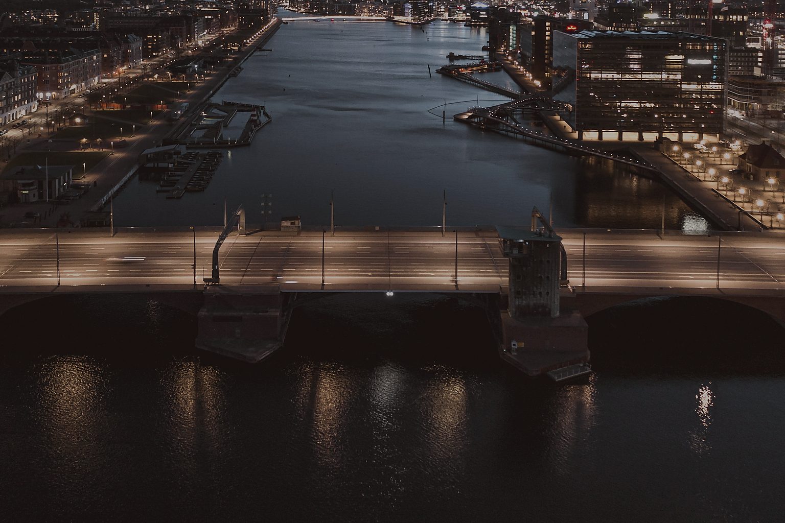 Copenhagen harbour seen from above at dusk with bridge, water, and lights along the quay.