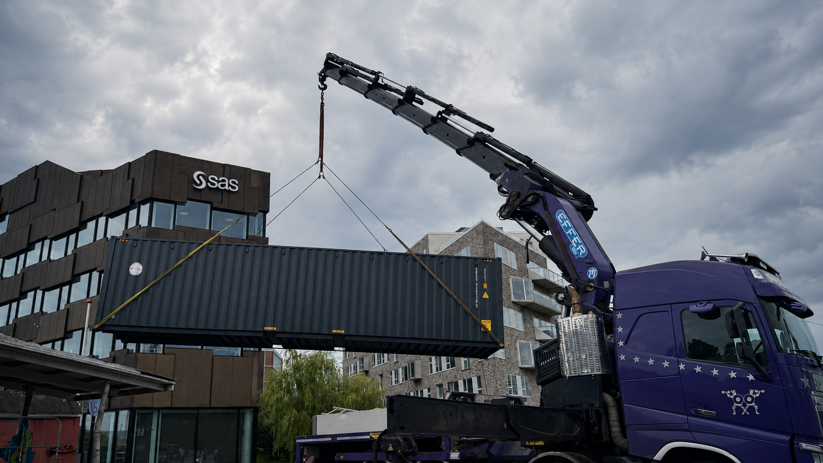 En antracitgrå 40-fods container hænger i løftestropper fra en kranbil under levering i Københavns Sydhavn.
